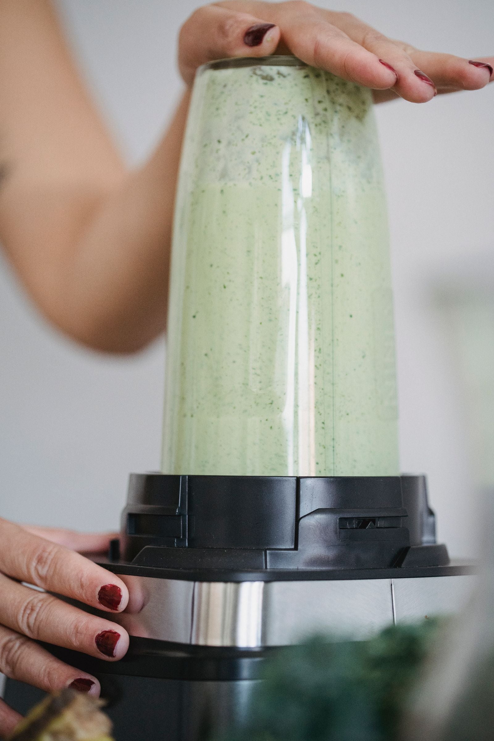 Hands blending a pale green smoothie in a personal blender